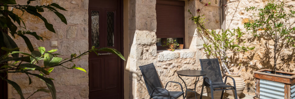 Αυλή με πετρόκτιστο κτίσμα με καρέκλες και ένα τραπέζι